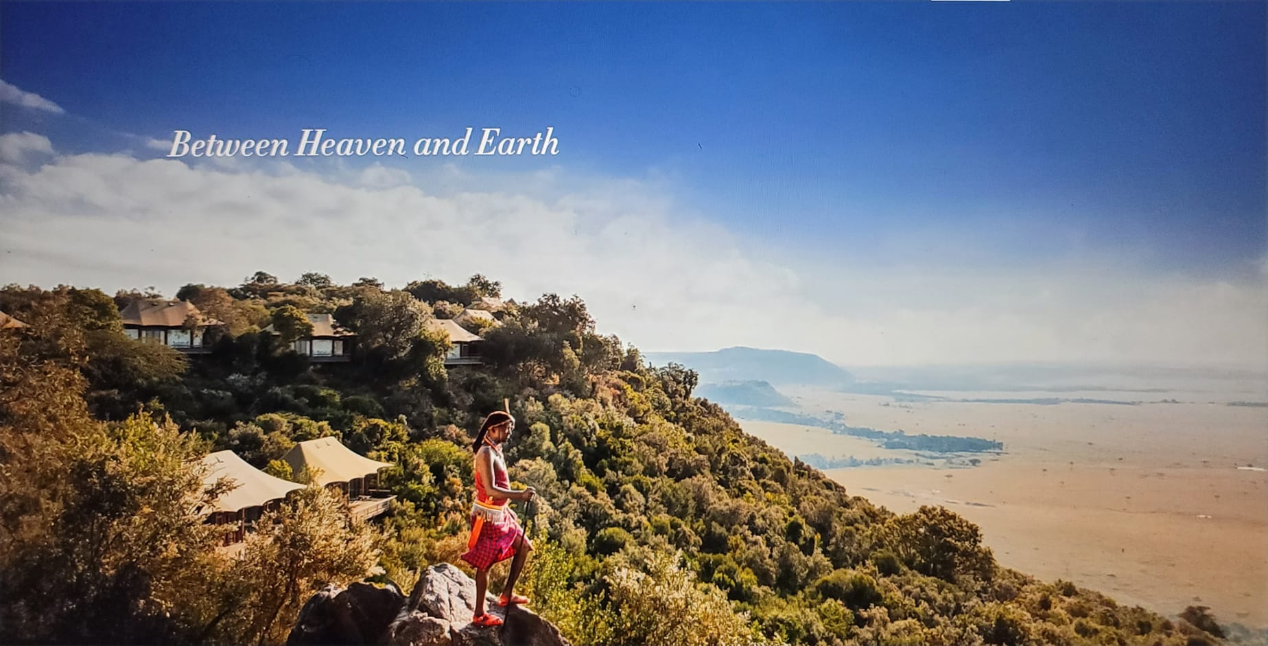 msasai standing on a cliff overlooking a vast landscape with 'Between Heaven and Earth' text.