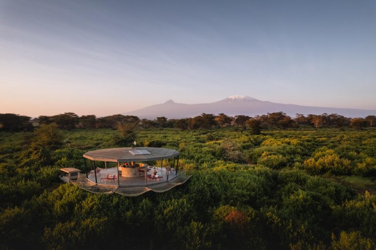 Modern glass pavilion in a lush green landscape with Mount Kilimanjaro in the background.