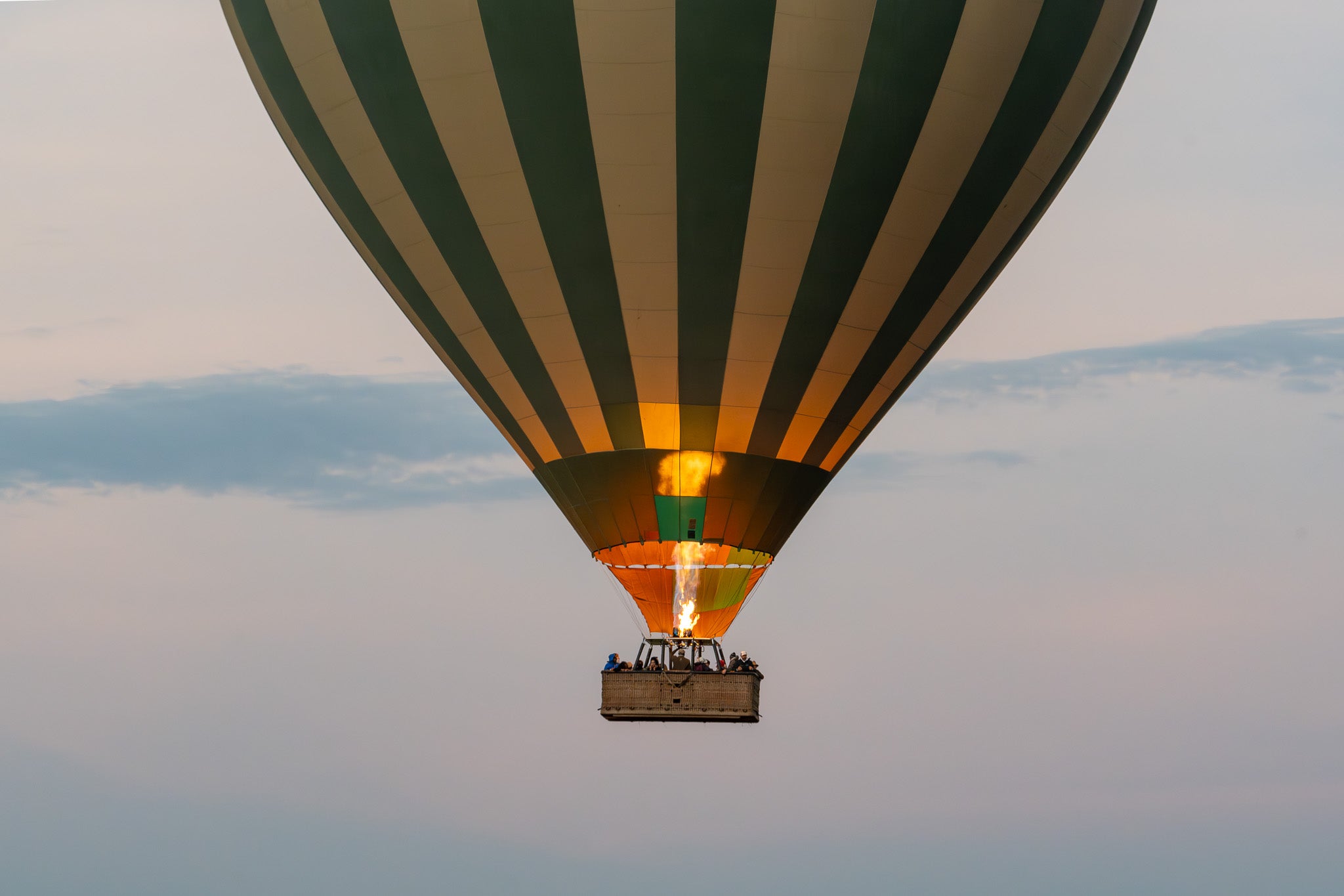 Hot air balloon with green and white stripes flying against a clear sky.