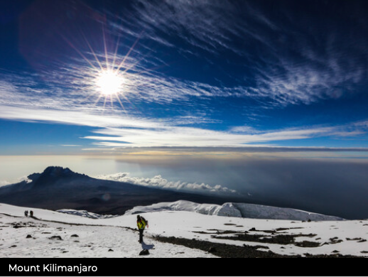 Person hiking on Mount Kilimanjaro with a bright sun and blue sky in the background