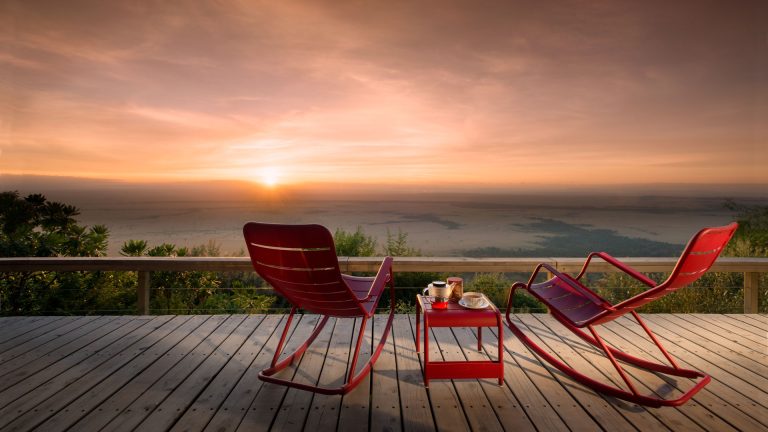Two red chairs on a wooden deck with a scenic sunset view.